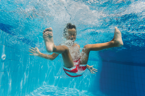 Cheerful little boy having fun diving in to the swimming pool