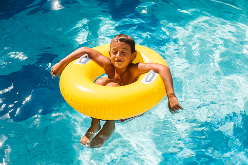 Boy enjoys the sun on inflatable ring  in the swimming pool