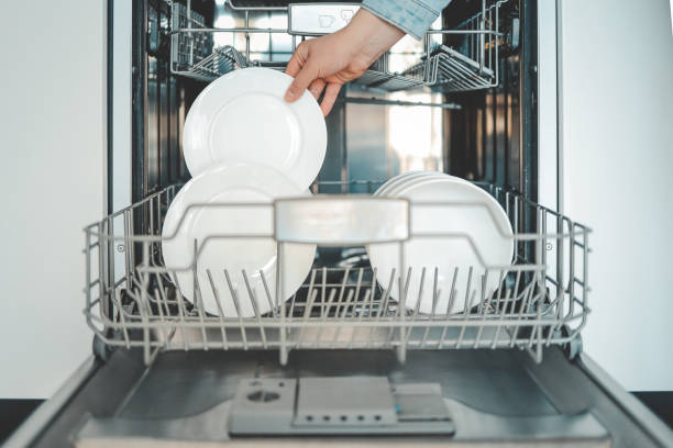 Female hand loading dished, empty out or unloading dishwasher with utensils. Kitchen appliances, lifestyle view. Woman puts a plate in the dishwasher or takes from it. Housewife does her housework. carga manual hembra de lavavajillas, vaciado o descarga de lavavajillas con utensilios. electrodomésticos de cocina, vista estilo de vida. la mujer pone un plato en el lavavajillas o lo toma de él. el ama de casa hace sus tareas domésticas