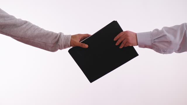 A woman passes a black folder on a white background to a man. A closeup in the frame of only hands and a folder. Transfer of classified information