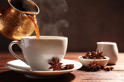 Pouring aromatic hot coffee into cup and anise stars on wooden table. Space for text