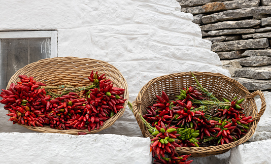 Two wicker baskets with fresh red and green peppers lie on a ledge of the white wall of a house in the city of Ostuni, Italy, close-up side view.