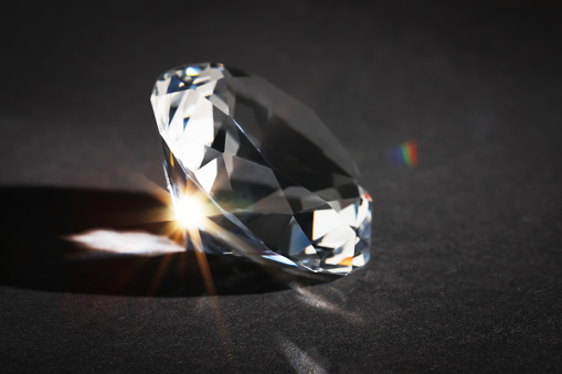 Beautiful dazzling diamond on dark background, closeup. Precious gemstone