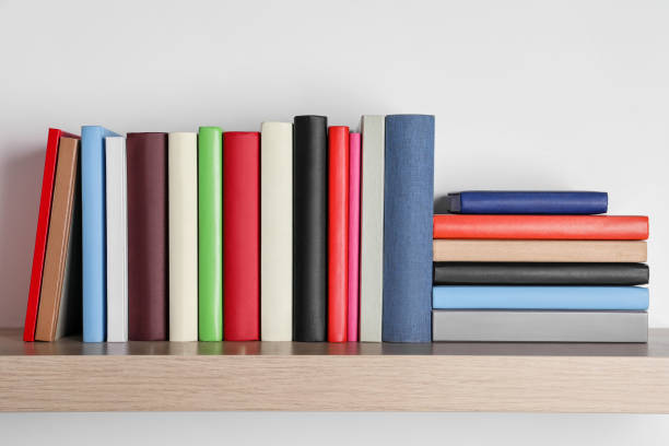 Different books on wooden shelf near white wall