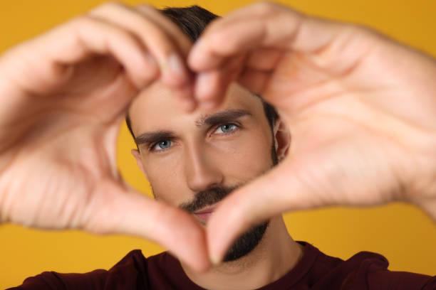 Man making heart with hands on yellow background, closeup