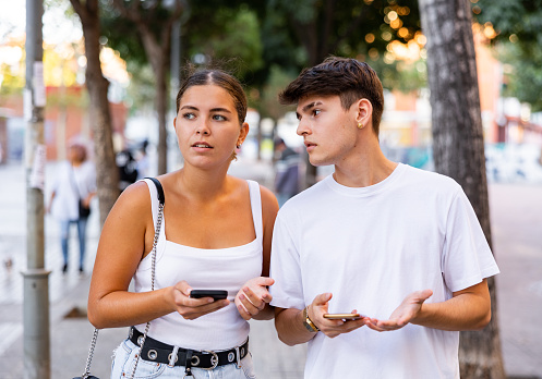 Modern young man and woman strolling together and phubbing