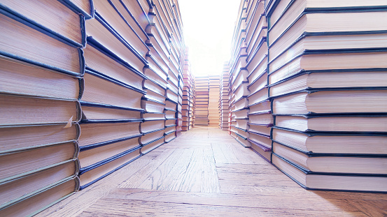 Stacks of books in the form of a long corridor on the old parquet  floor ultra wide angle view. Low angle high key image with selective focus