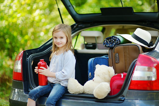 Adorable little girl with big teddy bear leaving for a car vacation with their parents