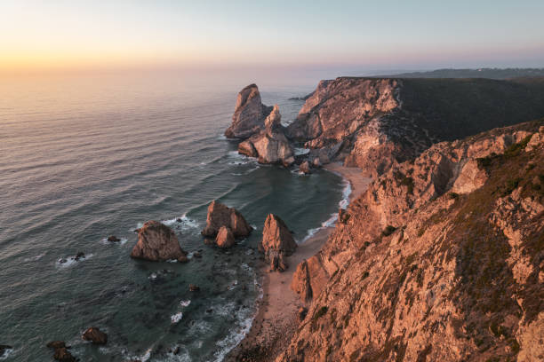 istock Wavy sea splashing on sandy beach near rocky cliffs at sunset 1478227690