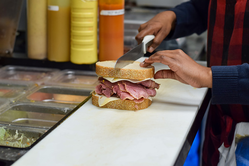 Hands of female diner restaurant employee cutting deli meat corned beef sandwich in half with a knife