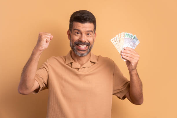 homem barbudo animado celebrando o dinheiro de negócios bem sucedido em fundo bege. finanças, investimento, oferta, conceito de empréstimo. - real people - fotografias e filmes do acervo