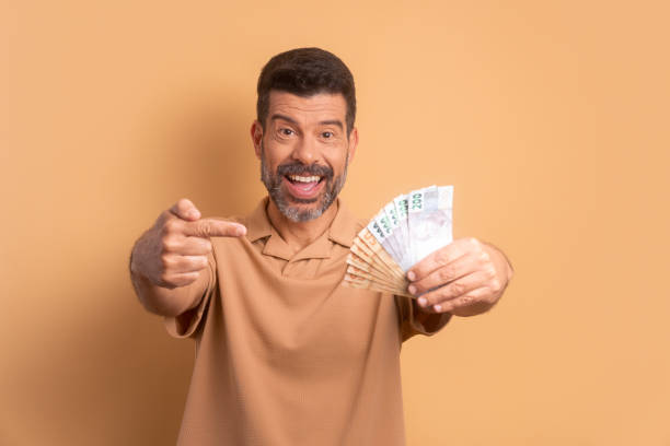 homme mature amusant avec des billets de banque brésiliens aux couleurs beiges. concept d’entreprise, de prêt, de paie, de patrimoine. - photography color image people real people photos et images de collection