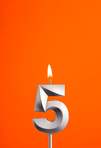 Number 5 - Burning anniversary candle on orange foamy background