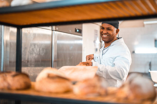 istock Mature Hispanic Baker Putting Freshly Baked Bread On A Rack In An Artisan Bakery 1478239712