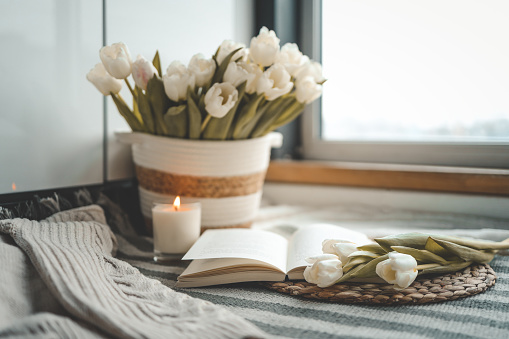 Open book, candle and basket with tulips, spring cozy composition in home interior.