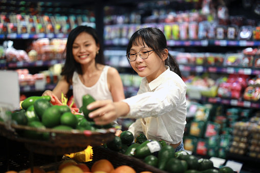 An Asian mother and daughter are shopping for fresh organic vegetables and fruits in a grocery store during the weekend, highlighting the concept of family bonding