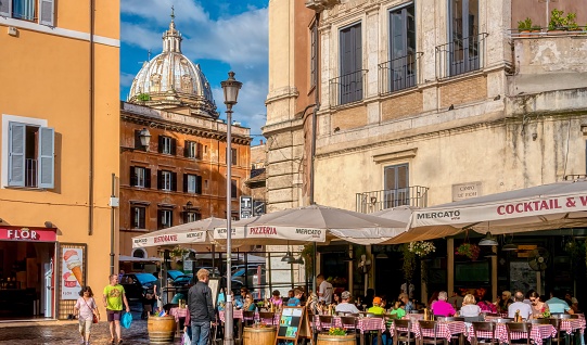 Rome, Italy - June 18, 2014. Tourists eating outdoors on tables with red and white checkered tablecloths at the Mercato Hostaria Restaurant in the Campo de Fiore, with the dome of the Sant'Andrea della Valle Basilica in the background.