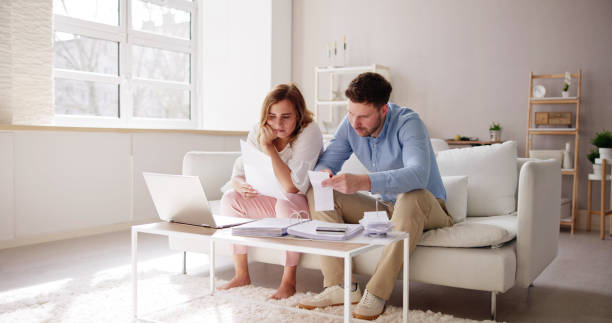 istock Shocked Young Couple Sitting On Sofa Looking At Bill 1478273535