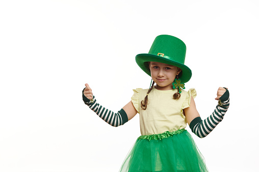 Adorable Irish little girl in Leprechaun carnival costume for St. Patrick's Day, thumbing up looking at camera, isolated on white background. Culture and traditions in Ireland. People and life events