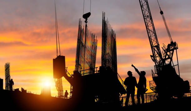 istock Silhouette of Engineer and worker checking project at building site background, construction site at sunset in evening time 1478285055