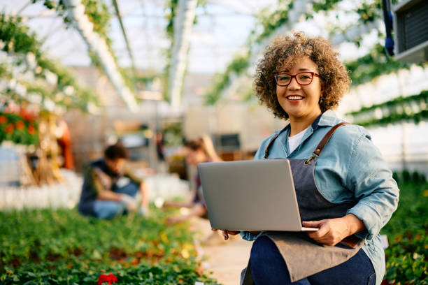 istock Happy woman using laptop while working in greenhouse and looking at camera. 1478288976