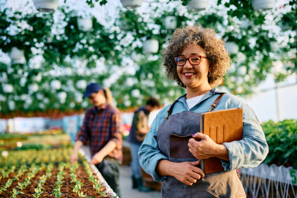 Portrait of happy plant nursery owner looking at camera. Happy small business owner at her plant nursery looking at camera. sustainable business stock pictures, royalty-free photos & images