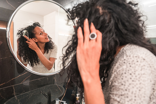Beautiful mid adult Hispanic female in a domestic bathroom. Looking at a mirror brushing her hair as part of a daily morning routine.