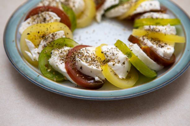 Slices of red, green and yellow tomatoes with slices of mozzarella and dusted with oregano displayed in a ring on a plate