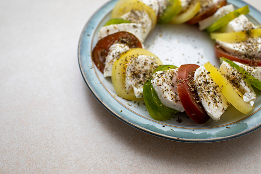 Slices of red, green and yellow tomatoes with slices of mozzarella and dusted with oregano displayed in a ring on a plate
