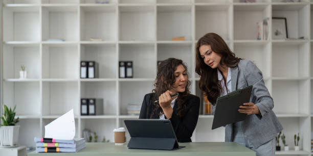 Two smart multiethnic business people working together with laptop while working on project in office