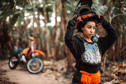 Young independent woman with curly hair put crash helmet on, wearing full dirt bike gear and protection,  Banana Island, Hanoi