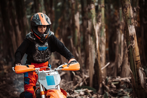 Young independent woman ride an orange dirt bike through narrow paths and dusty roads in a tropical forest, wearing full dirt bike gear and protection,  Banana Island, Hanoi