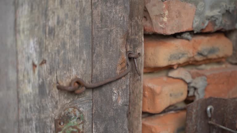 The old wooden door of a brick building is closed with an iron hook. Smooth camera movement