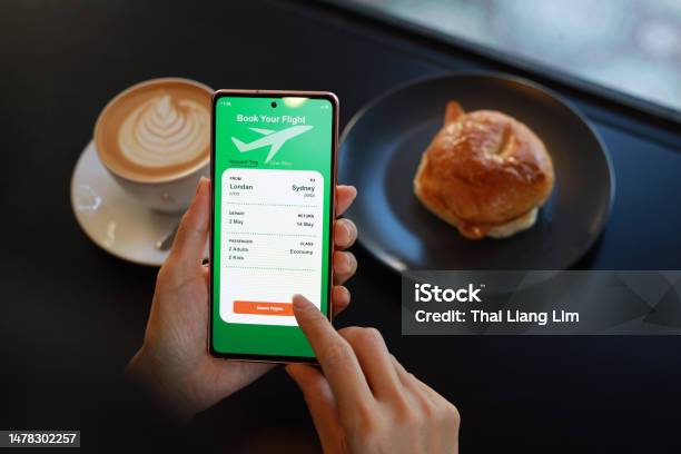 Cropped Shot Of A Woman Is Using A Smartphone Application To Book Flight Tickets And Plan Her Holiday While Having Breakfast In A Cafe Stock Photo - Download Image Now