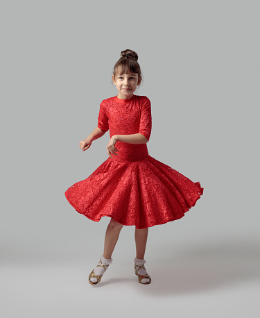 Dancing girl in a red dress on a grey background.