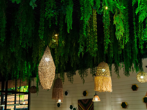chandeliers with rattan shades and fringes and many suspended artificial plants on the ceiling of the cafe