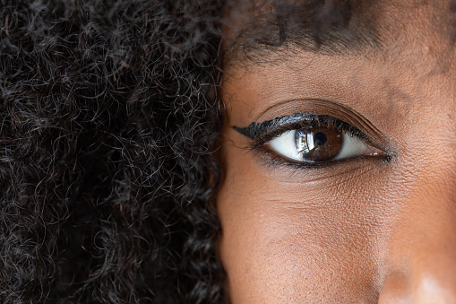 Macro of the human eye of an African woman wearing makeup with an afro hairstyle. Large black copy space on the hair and eye details with eyelashes and eyebrows treated by the beautician.