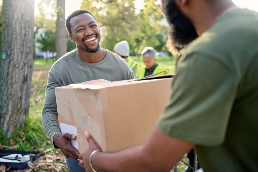 Black man, volunteering and giving box in park of donation, community service or social responsibility. Happy guy, NGO worker and helping with package outdoor for charity, support or society outreach