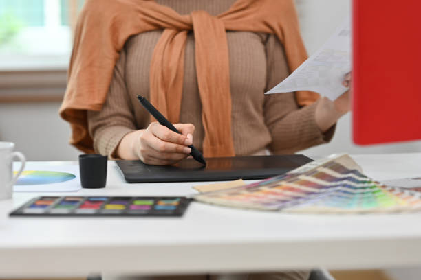 istock Young creative woman using graphic tablet and working with color swatch samples at workstation. 1478310441