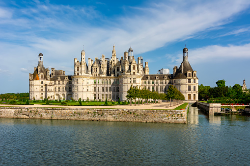 View of Gien cityscape on bank of Loire with row of townhouses along embankment, medieval renaissance castle and arched bridge across river on summer day, Loiret, France