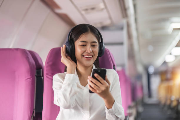 веселая женщина-пассажир в наушниках для шумоподавления смотрит онлайн фильм во время межконтинентального перелета в салоне самолета, сча - room service audio стоковые фото и изображения