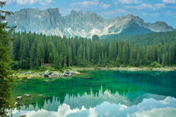 lac carezza un lac alpin entouré de haute forêt de pins dans les dolomites avec le fond de vue de chaîne de montagne de rosengarten dans le tyrol du sud, italie - latemar mountain range photos et images de collection