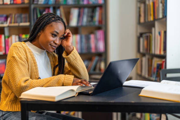 istock Young woman using laptop, sitting at desk in a library. 1478315990