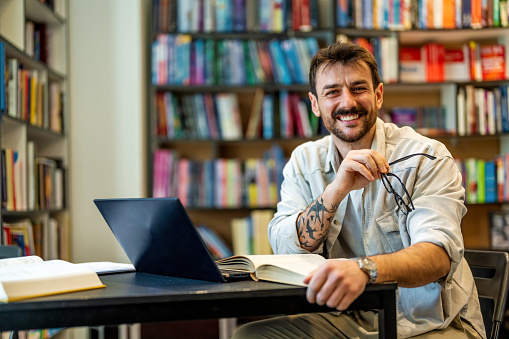 Confident male scientist satisfied with intellectual work in public library looking at camera