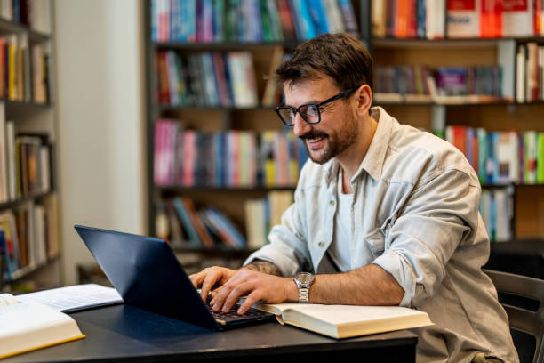 istock Handsome male student in a university library working on laptop. Young man studying on school assignment. 1478316090