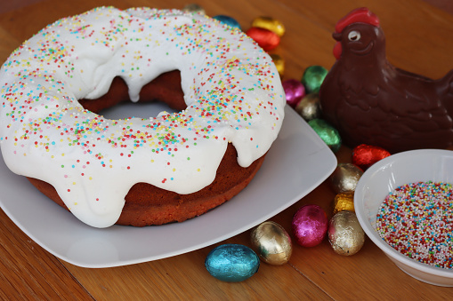 Ciaramicola. Traditional italian Umbrian cake for Easter. Red donut-shaped cake, made with Alchermes and decorated with white sugar glaze and multicolored sprinkles near a chocolate hen