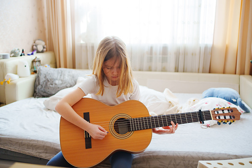 cute little girl learning to play teen guitar. self-study of playing musical instruments, online lessons in a music school.