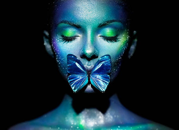 Fashion model woman in bright sparkles and neon lights posing in studio. Portrait of beautiful woman with butterfly. Art design glitter glowing make up