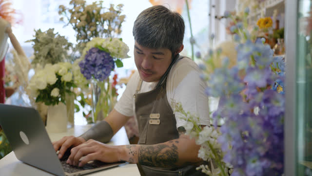 Small business asian owner man with labtop computer using mobile phone at flower shop.