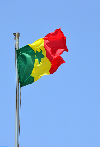 Dakar, Senegal: Senegalese flag flying in the wind of the Atlantic against clear blue sky - The flag of the Republic of Senegal, adopted in 1960 following Senegal's divorced from Mali - three vertical and equal bands in green, gold and red. A green five-pointed star sits in the center of the gold band.